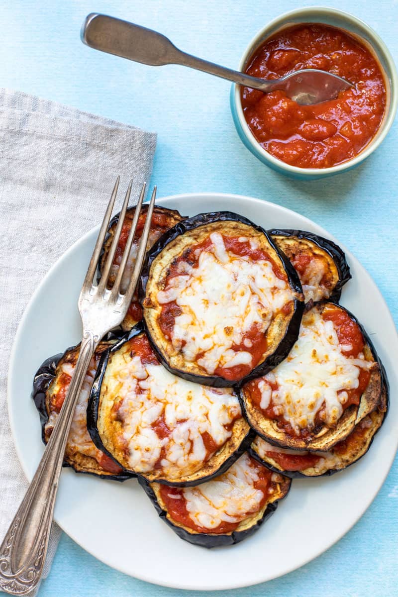 plate of eggplant parmesan with fork and napkin and small bowl of tomato sauce