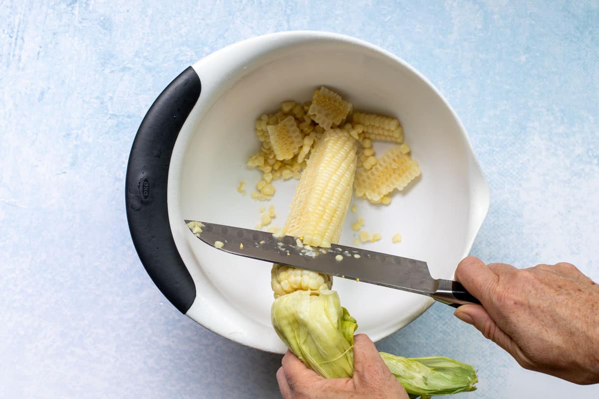 cutting corn off the cob using chef's knife and large bowl