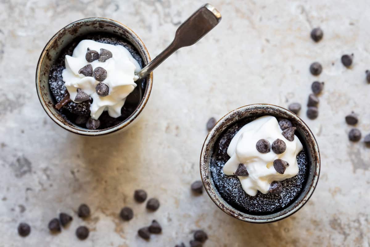 two mugs of chocolate almond flour mug cake topped with whipped cream and chocolate chips
