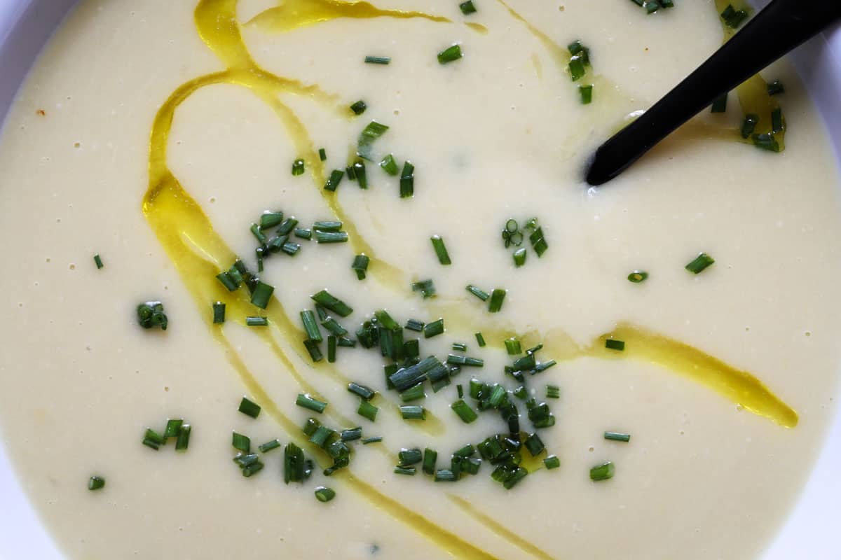 close up of bowl of vegan potato leek soup topped with a drizzle of oil and chopped chives
