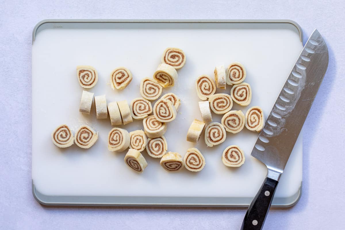 Sliced cinnamon swirls on cutting board with knife. 