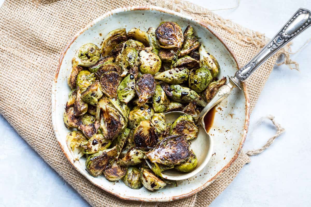 plate and serving spoon with balsamic-glazed Brussels sprouts sitting on top of folded burlap
