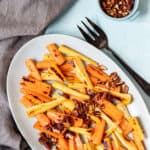 platter of roasted carrots and parsnips next to napkin, serving fork, and bowl of pecans