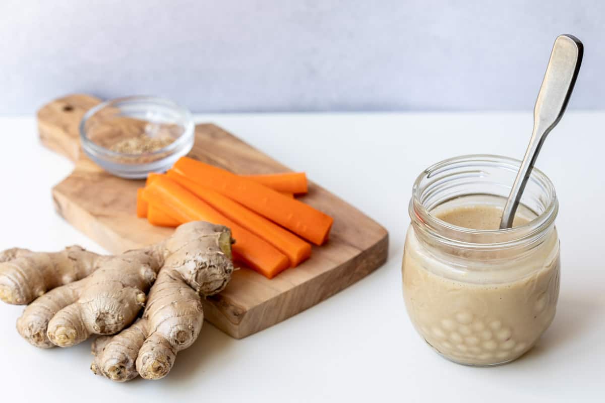 jar of sesame ginger dressing next to cutting board with carrots, ginger, and sesame seeds. 