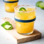 passion fruit margarita on a cutting board next to jalapeno slices, in front of another margarita glass