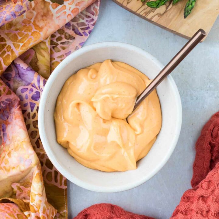 bowl of sriracha aioli with spoon surrounded by brightly colored kitchen towels