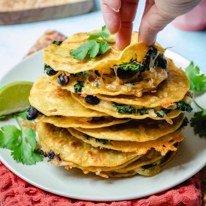 stack of corn tortilla quesadillas on plate with hand pulling up top tortilla on top quesadilla