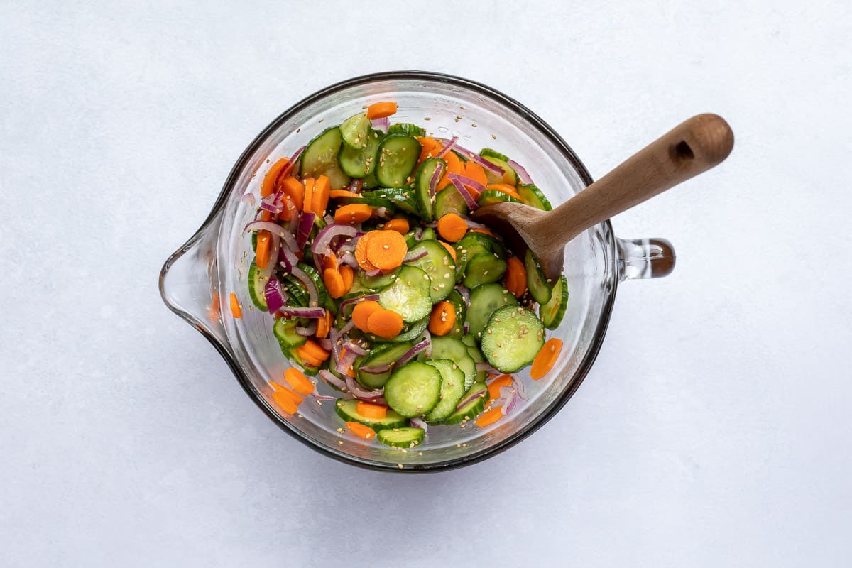 cucumber carrot salad in glass bowl with dressing and sesame seeds added