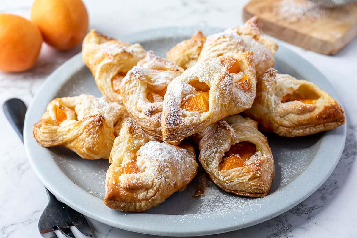 plate of apricot danishes next to serving fork and two apricots