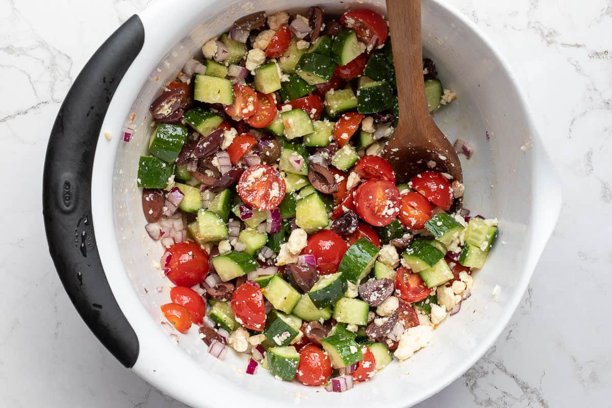 mixing bowl with cucumbers, tomatoes, olives, red onion, and feta cheese