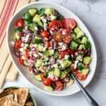 bowl of mediterranean cucumber tomato salad next to bowl of pita chips and napkin