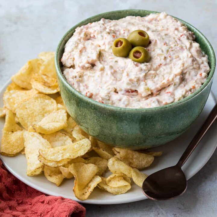 olive dip in bowl next to potato chips, spoon, and red napkin