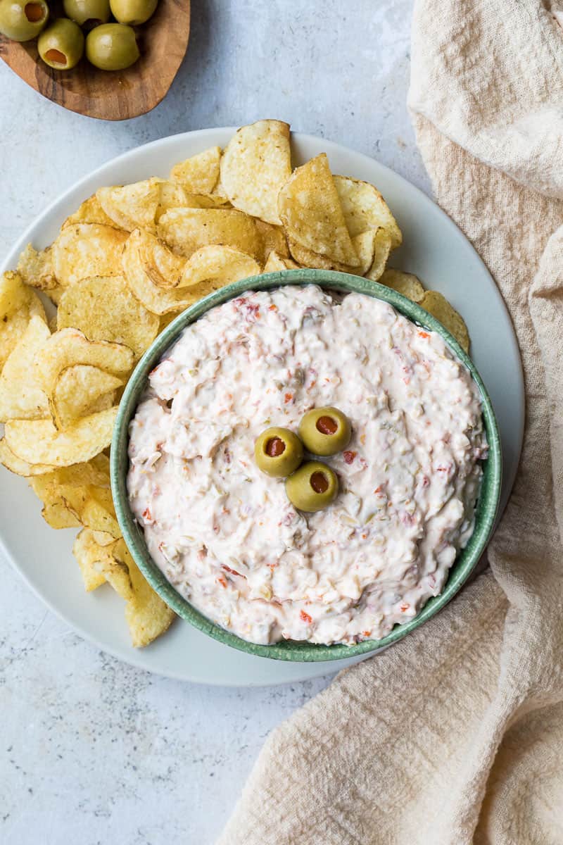 olive dip in bowl next to potato chips and linen towel and bowl of olives