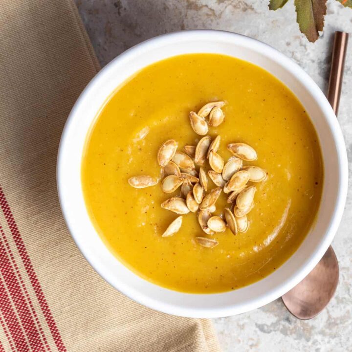 pumpkin soup without cream topped with pumpkin seeds next to napkin and spoon