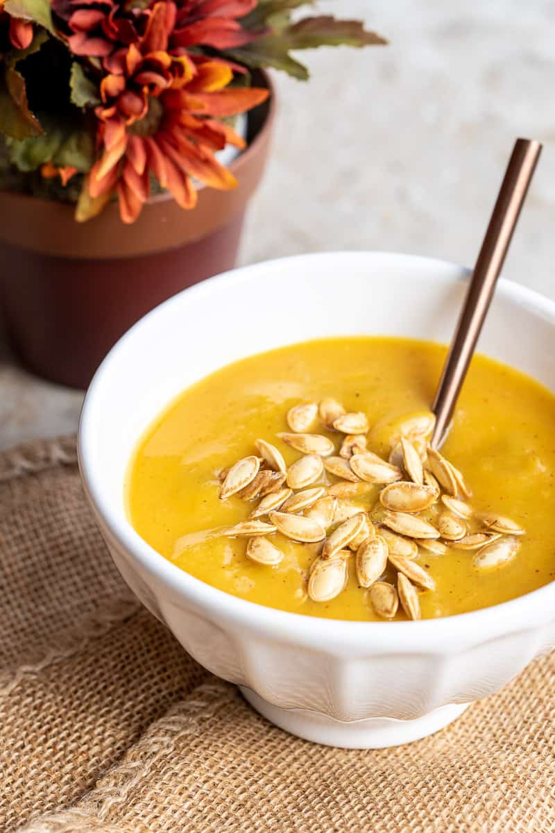 pumpkin soup topped with pumpkin seeds in bowl on burlap in front of flowers