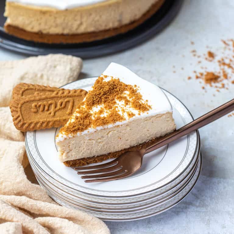 slice of biscoff cheesecake on stack of small plates with fork and biscoff cookies.