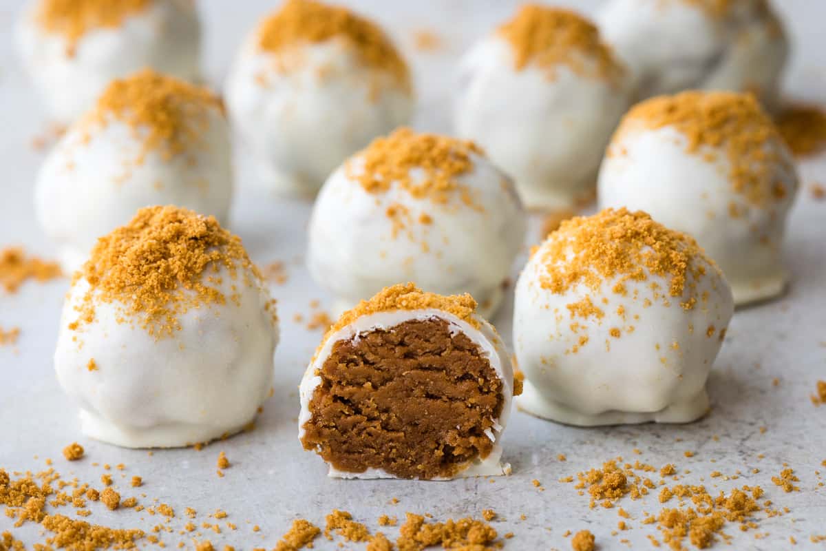 close up of half of a biscoff truffle in front of a bunch of other biscoff truffles with biscoff crumbs all around.
