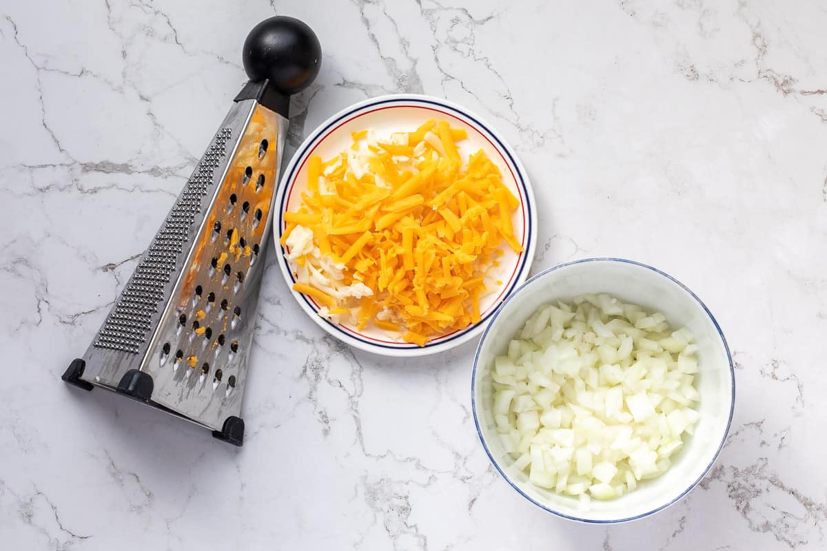 grated cheese and chopped onion in bowls next to grater.