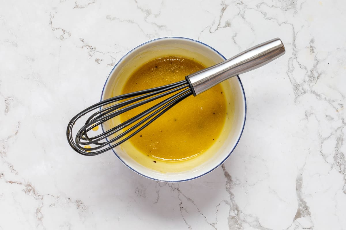 maple vinaigrette dressing in small bowl with whisk balanced on top.