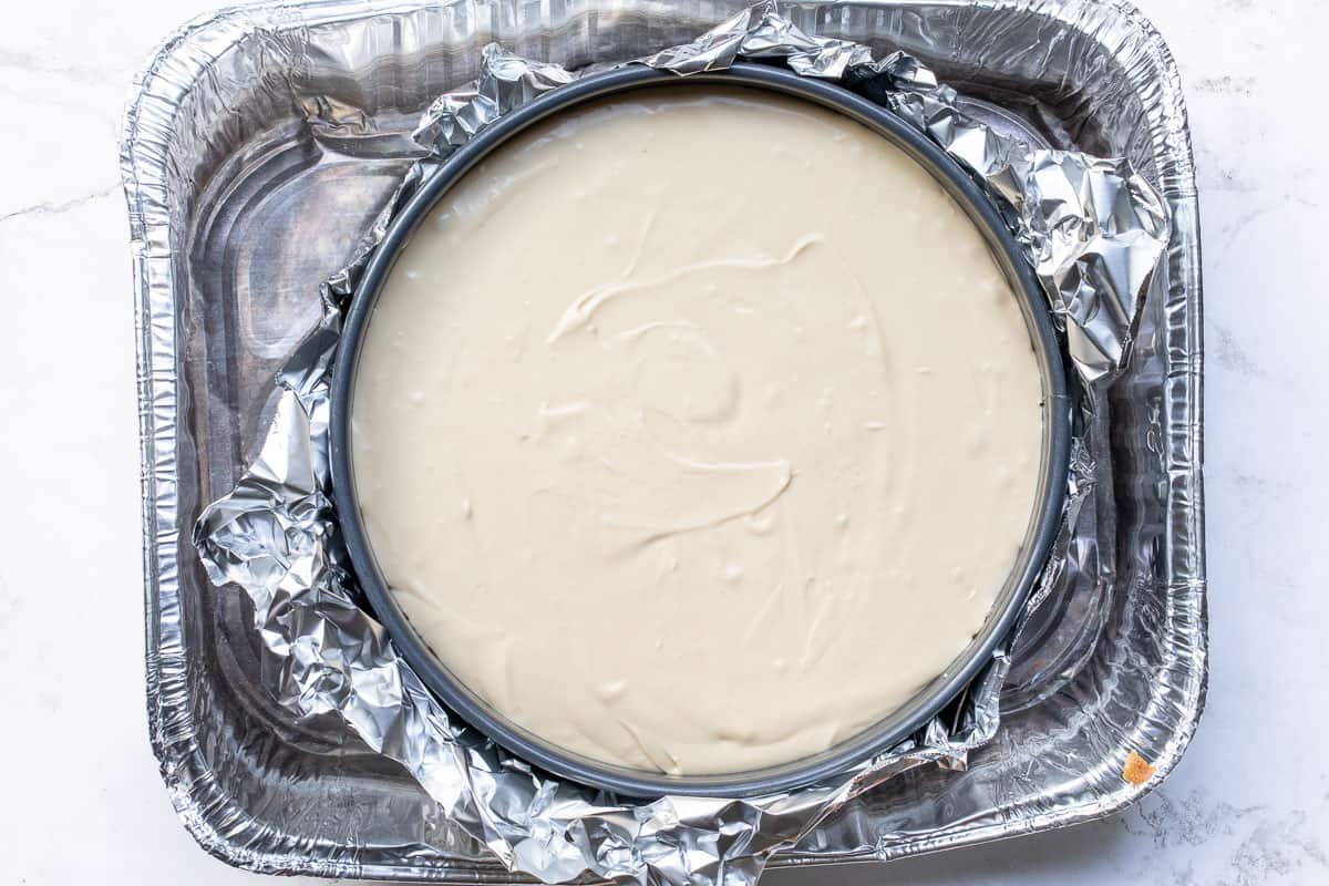 cheesecake in pan wrapped in foil in larger roasting pan.