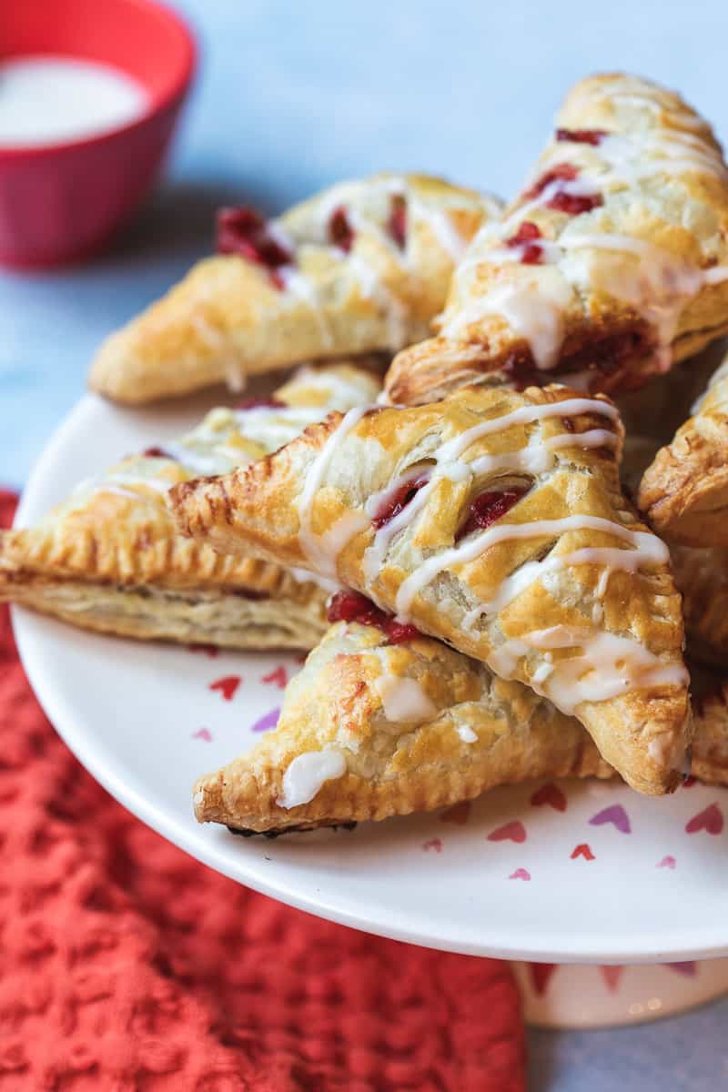 baked strawberry turnovers drizzled with glaze on top of serving platter next to napkin.