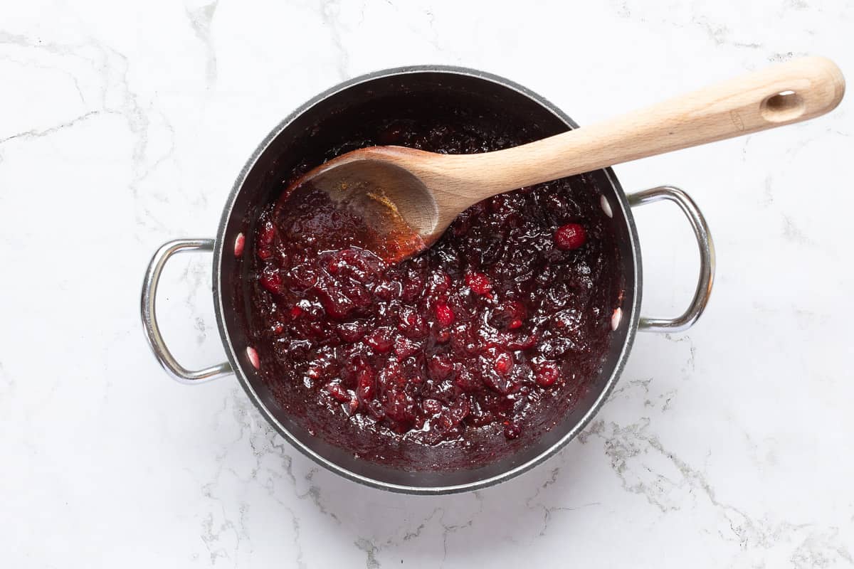 fresh cranberry sauce in saucepan with wooden spoon.