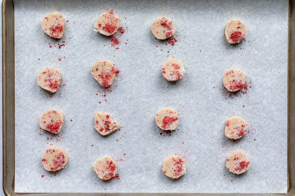 sliced strawberry shortbread cookie dough on sheet pan covered with sugar and dried strawberries.