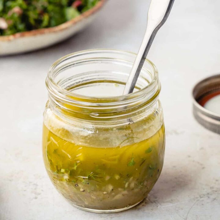 jar of honey lime dressing with spoon in front of salad plate and next to jar lid.