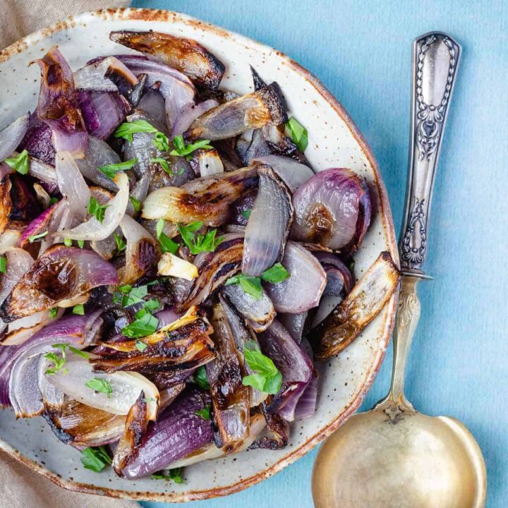 shallow bowl with roasted red onions next to serving spoon and linen.