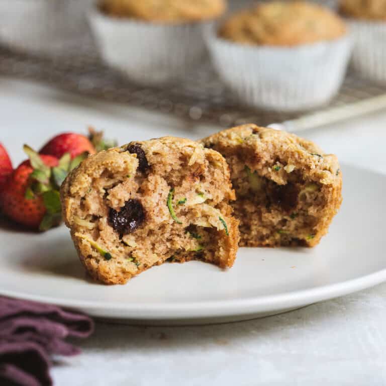 close-up of two halves of almond flour zucchini muffin on plate next to strawberries.