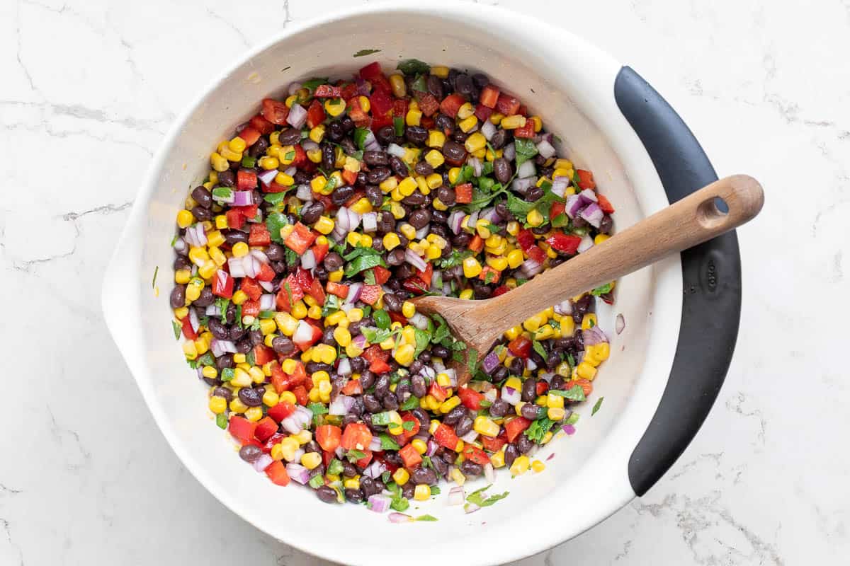 mixing bowl with black bean and corn salsa and wooden spoon.