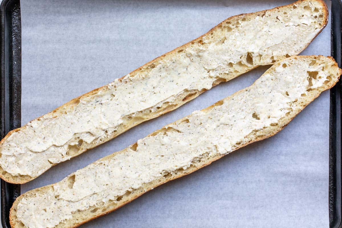 baguette halves spread with garlic butter on parchment-lined sheet pan.