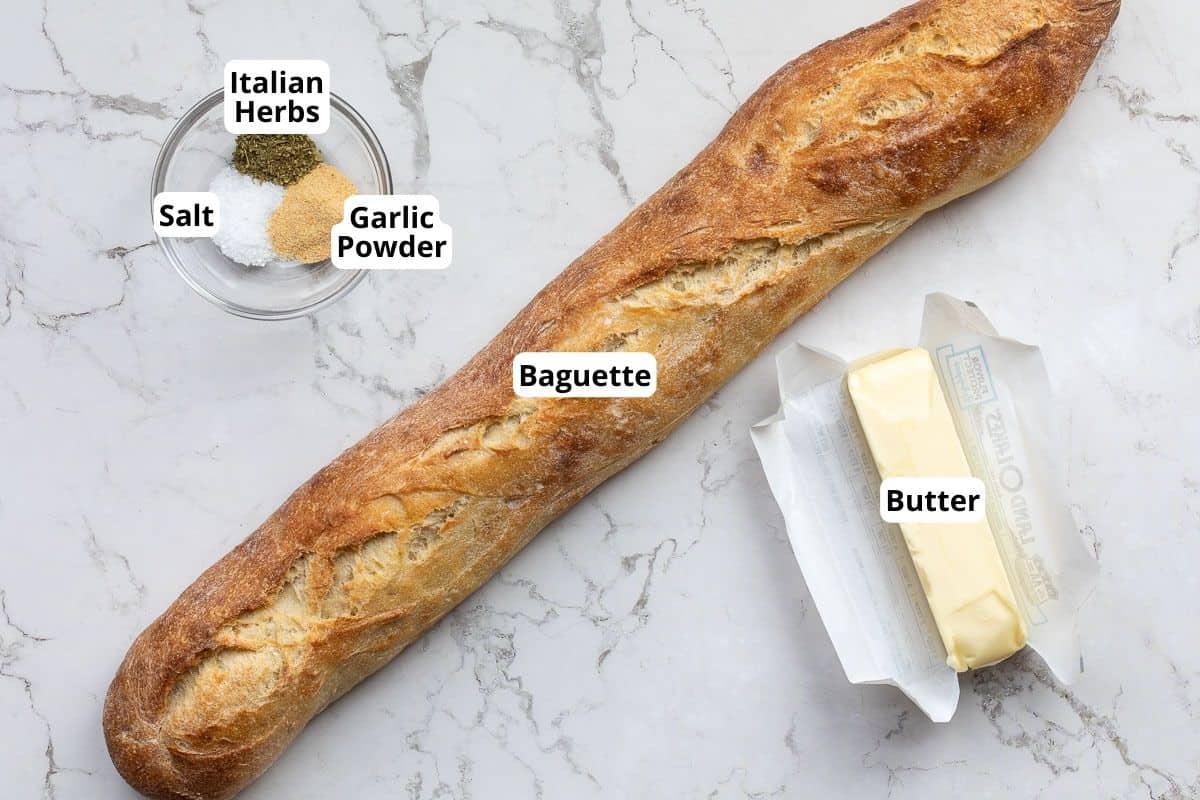 bowl with salt, Italian herbs, and garlic powder next to baguette and stick of butter.
