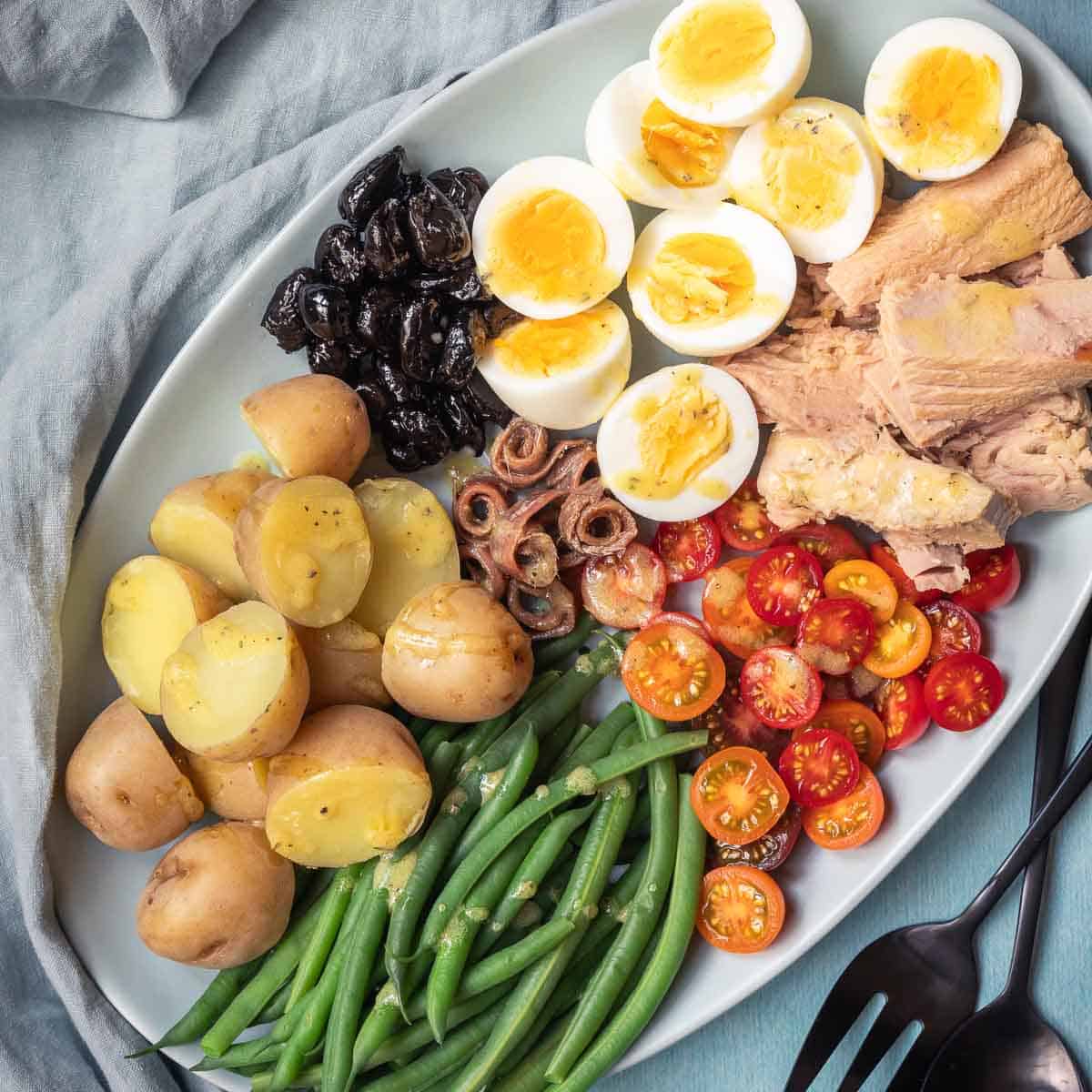 Niçoise salad with tuna, green beans, and potatoes next to blue napkin and serving utensils.