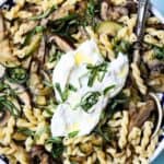 bowl of zucchini mushroom pasta with burrata cheese and basil with serving spoon in bowl.