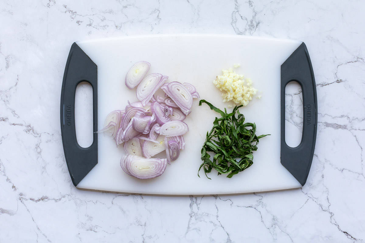 sliced shallots and basil next to minced garlic on cutting board.