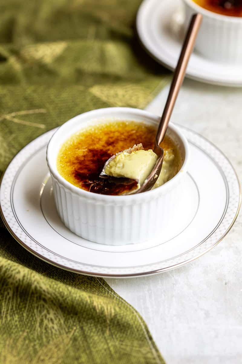 ramekin of matcha crème brûlée with spoon on small plate in front of other plate and next to napkin.