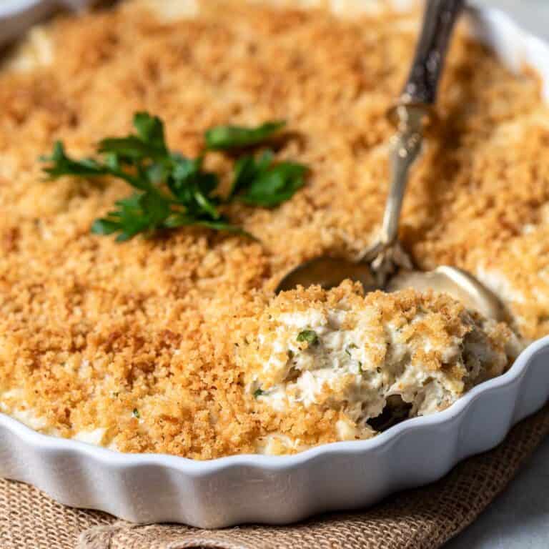spoon scooping a portion of hot crab dip out of baking dish with crab dip topped with parsley.