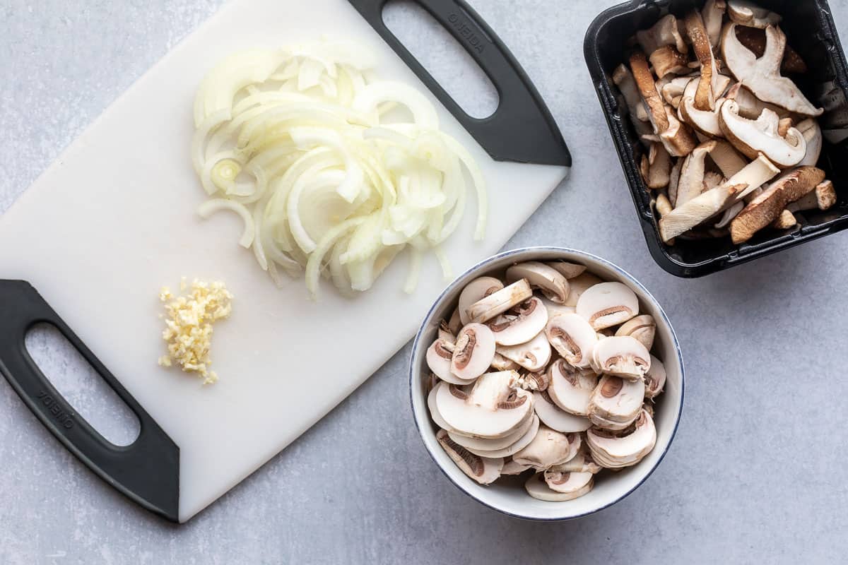 sliced onions and mushrooms and minced garlic on cutting board.