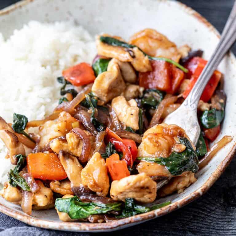 shrimp and chicken stir fry on plate with fork holding shrimp with spinach.