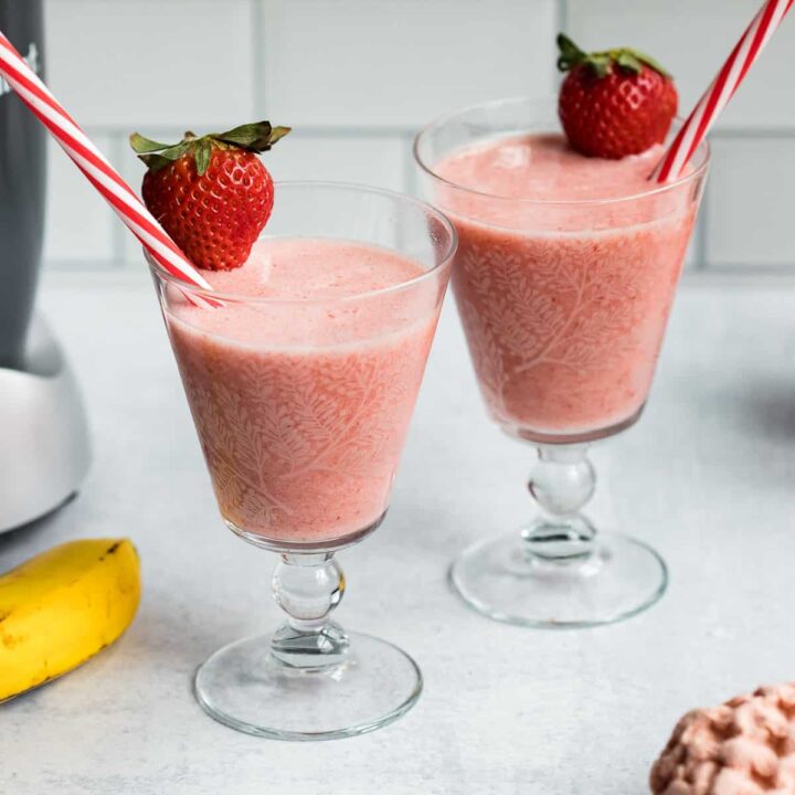 two glasses filled with non-dairy strawberry banana smoothie with straws.