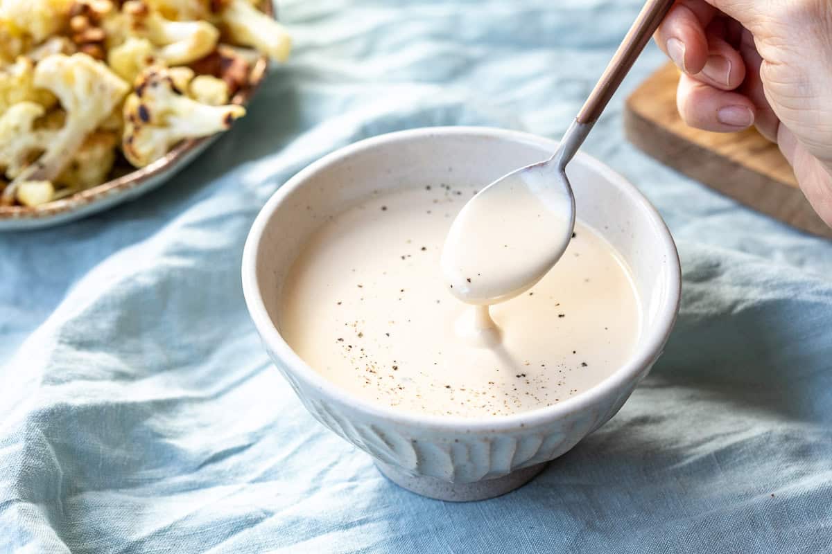 bowl of tahini yogurt sauce with spoon showing it dripping off.