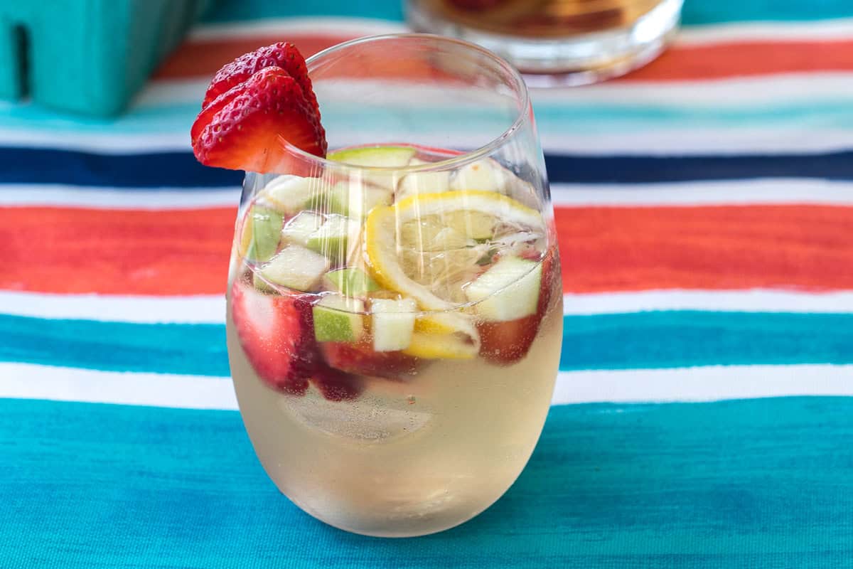 glass of white wine sangria with strawberries, apples, and lemon slices.