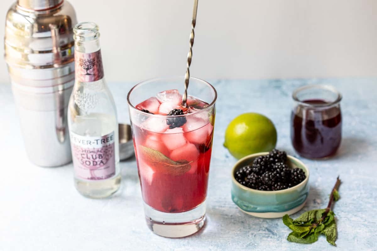 blackberry mojito with club soda, bowl of blackberries, lime, and mint.