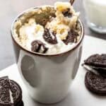 oreo mug cake topped with crushed Oreos and whipped cream next to Oreos.