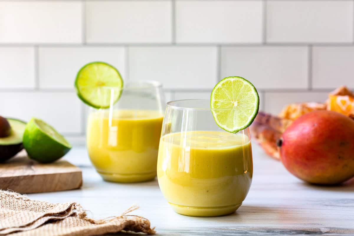 two mango avocado smoothies with lime slices next to mango and limes.