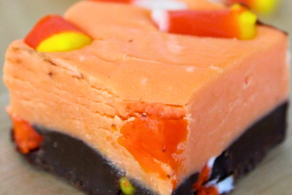 A square piece of layered fudge with an orange top, a dark chocolate base, and pieces of candy corn mixed in.