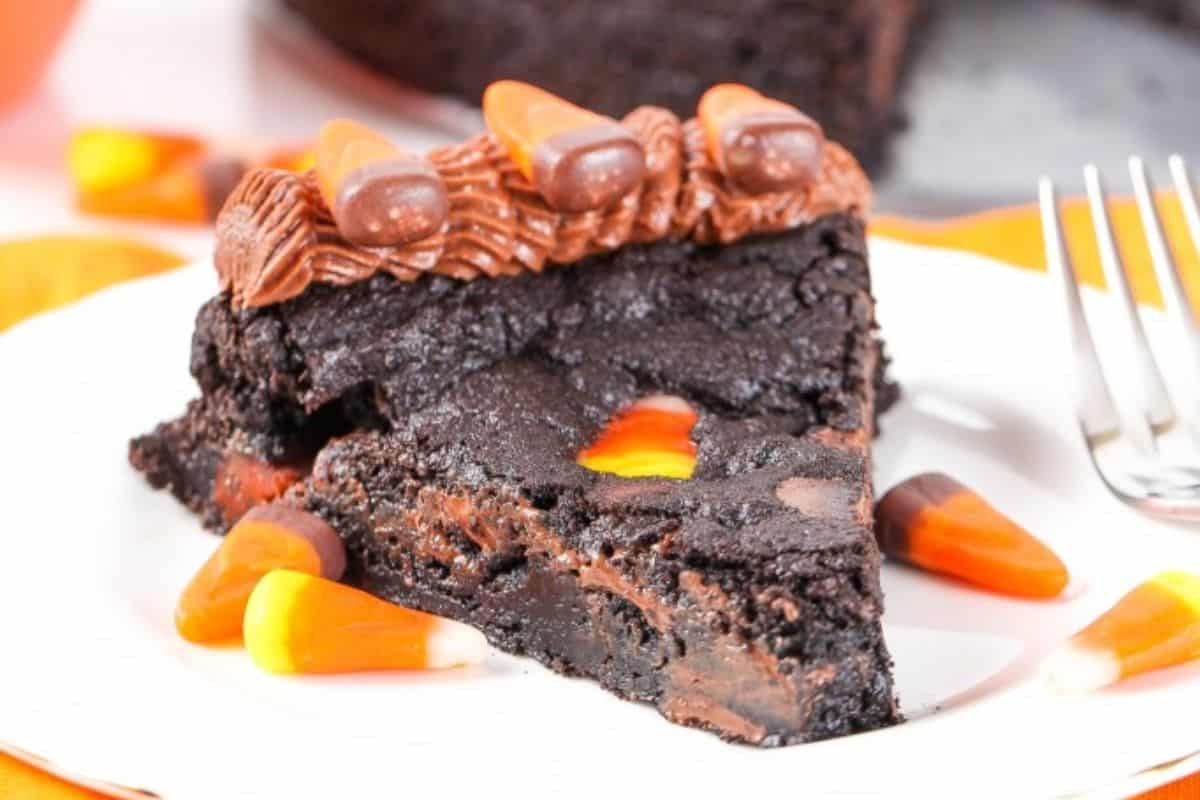 A slice of chocolate cake on a white plate, decorated with chocolate frosting and candy corn pieces.