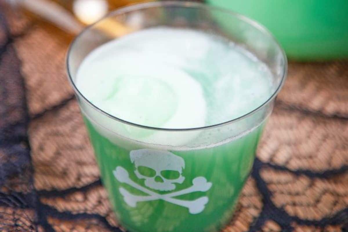 A glass filled with green beverage and ice cream, decorated with a white skull and crossbones symbol.