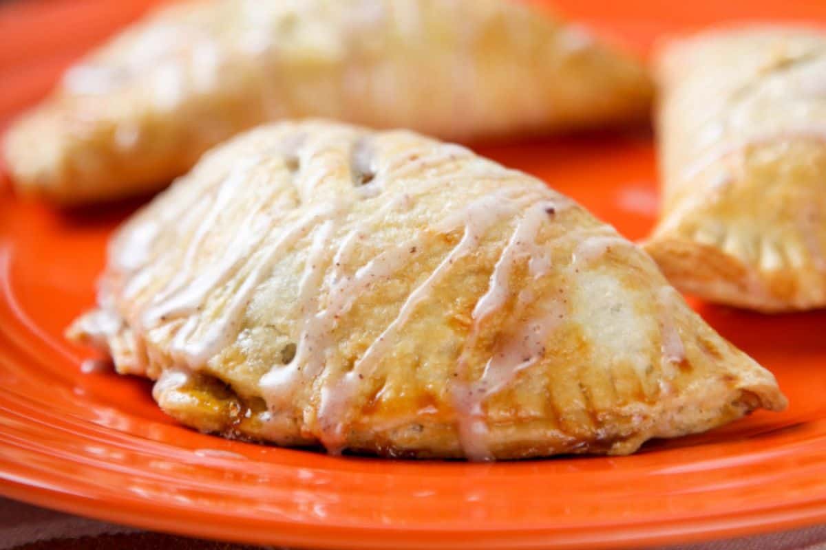 Three glazed hand pies, perfect as spooky desserts, are arranged on an orange plate.